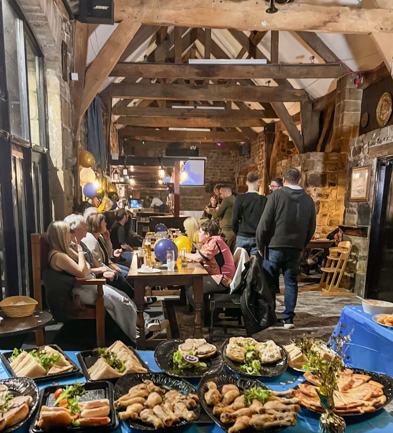 A rustic dining setting with people enjoying food and drinks at wooden tables.