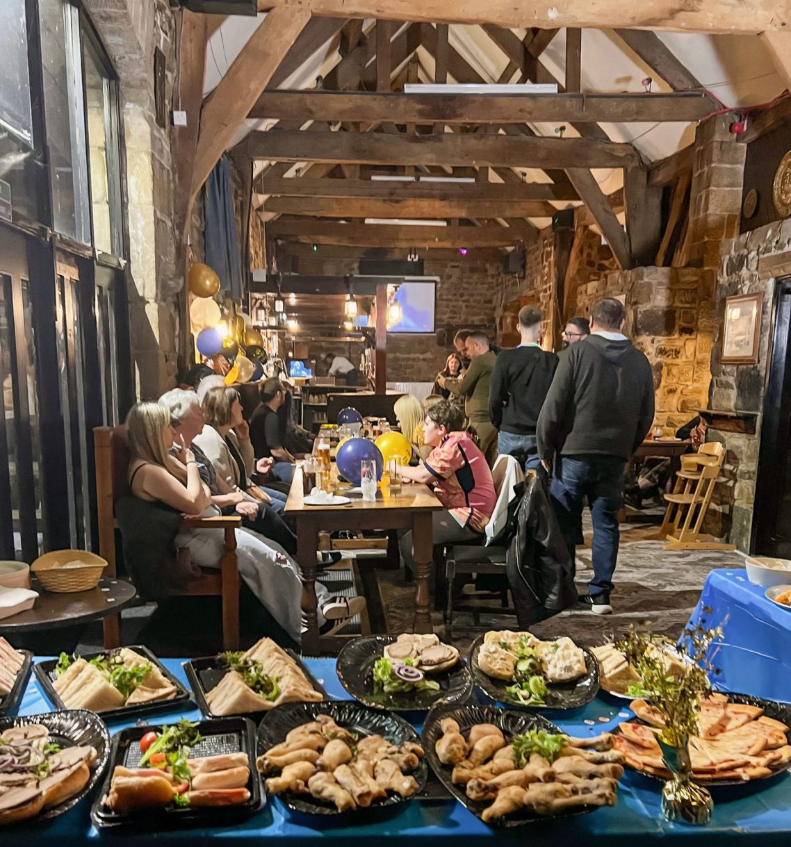 A rustic dining setting with people enjoying food and drinks at wooden tables.